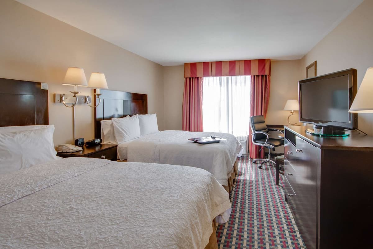 A hotel room with two beds, a desk, a television, and a desk lamp.