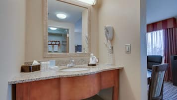 Baño de hotel con lavamanos de encimera de granito, un espejo grande, un secador de pelo y un perchero para toallas.