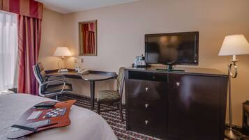 A hotel room with a bed, a desk with a chair, a television, a lamp, and a minibar.