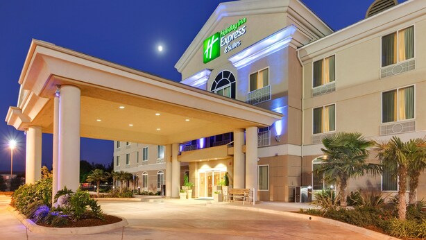 A Holiday Inn Express & Suites with a covered entrance, palm trees, and a well-lit facade.