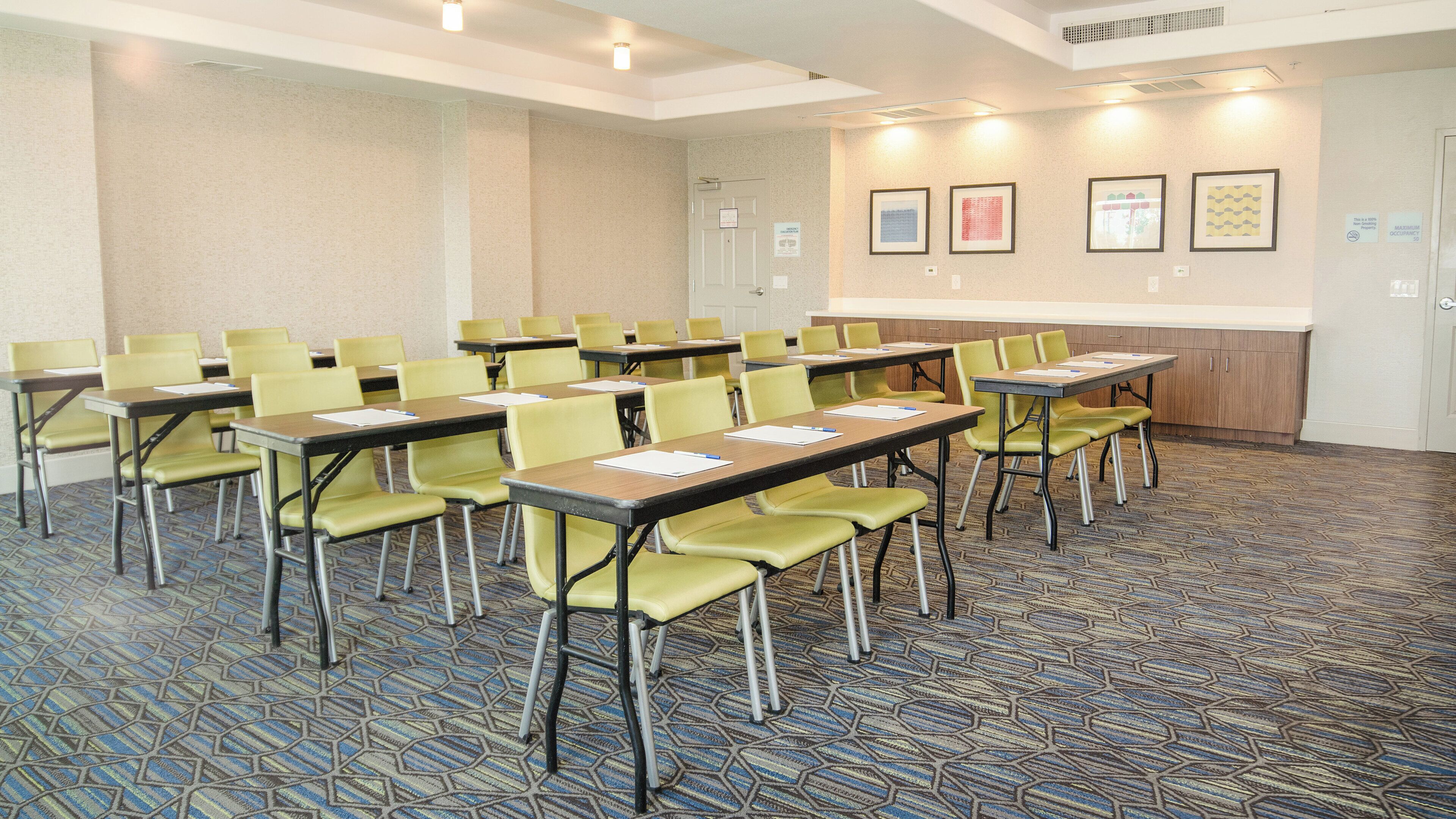 Une salle de conférence dotée de plusieurs tables et chaises, d’un tapis à motifs et de tableaux encadrés accrochés au mur.