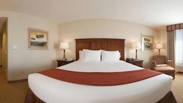 Habitación de hotel con una cama grande, dos mesitas de noche con lámparas, una silla y dos cuadros en las paredes.