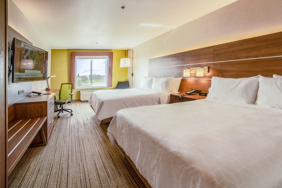 A hotel room with two beds, a desk, a chair, a TV, and a window with curtains.
