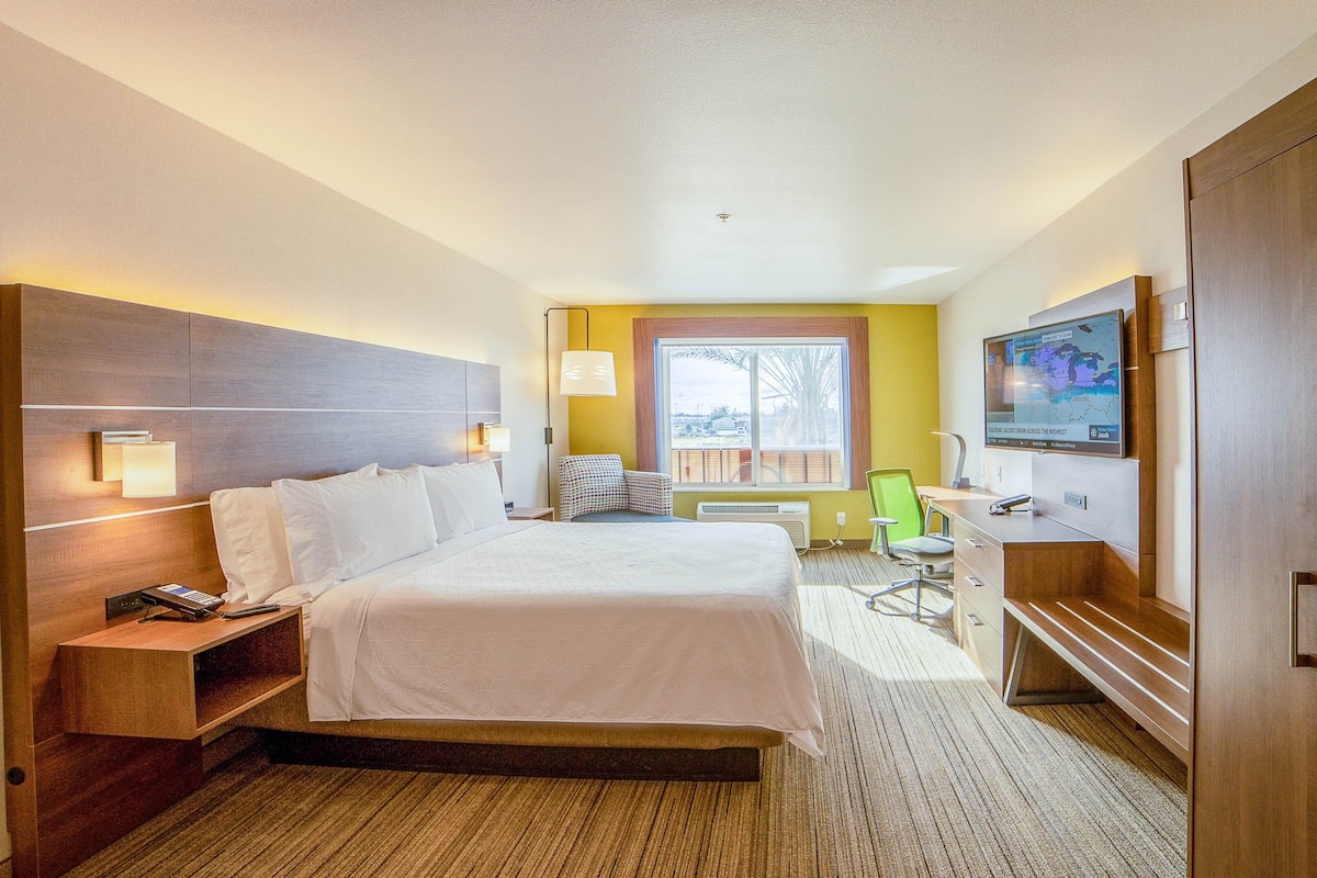 A hotel room with a large bed, bedside tables, a desk with a chair, a television, and a window with a view.