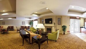 A spacious lobby with a fireplace, comfortable seating, a television, and a carpeted floor.