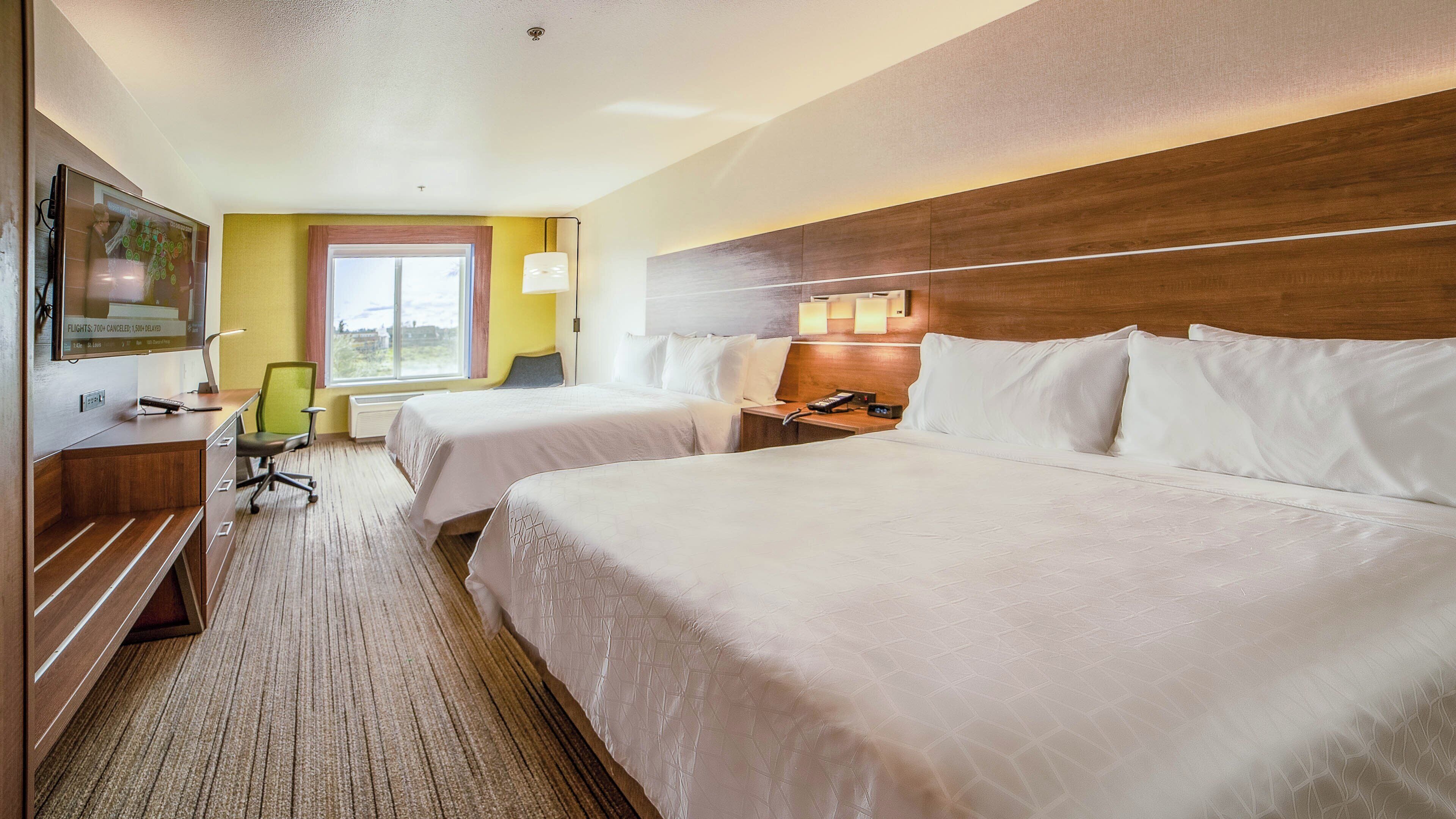 A hotel room with two beds, a desk, a chair, a TV, and a window with curtains.
