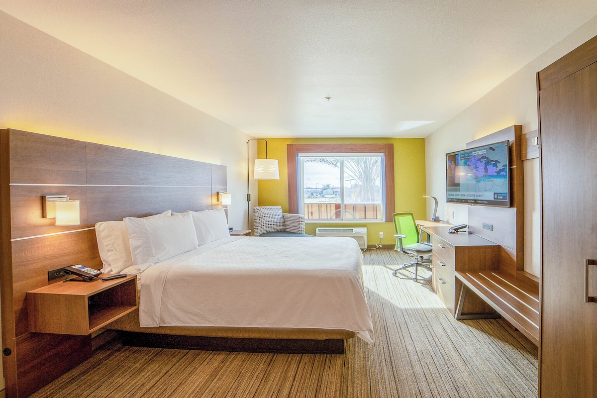 A hotel room with a large bed, bedside tables, a desk with a chair, a television, and a window with a view.
