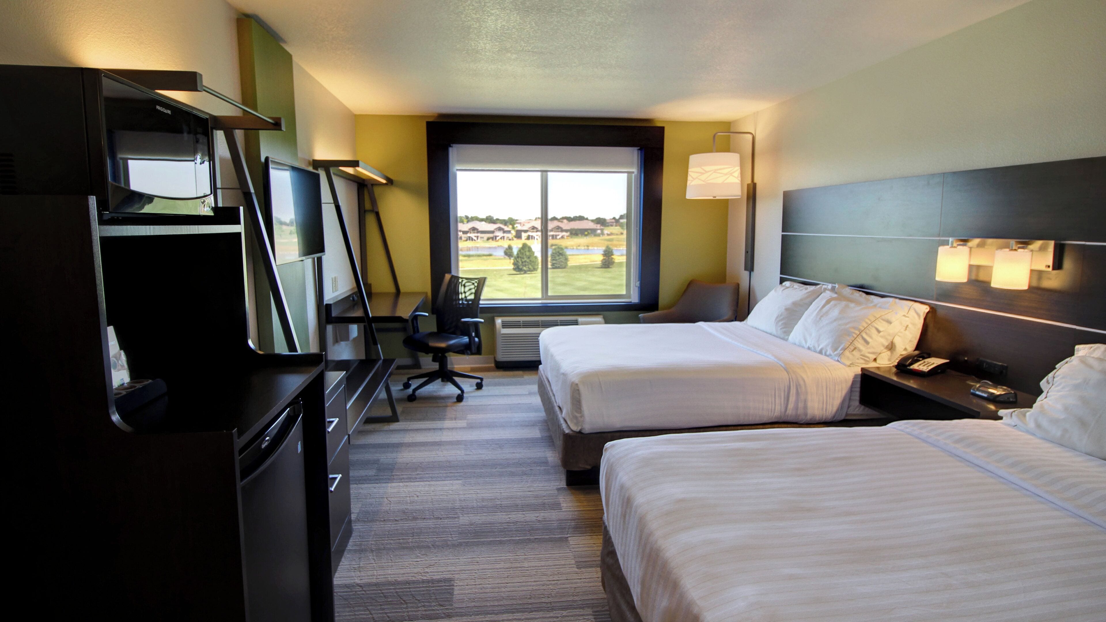 A hotel room with two beds, a desk, a chair, and a large window with a view.
