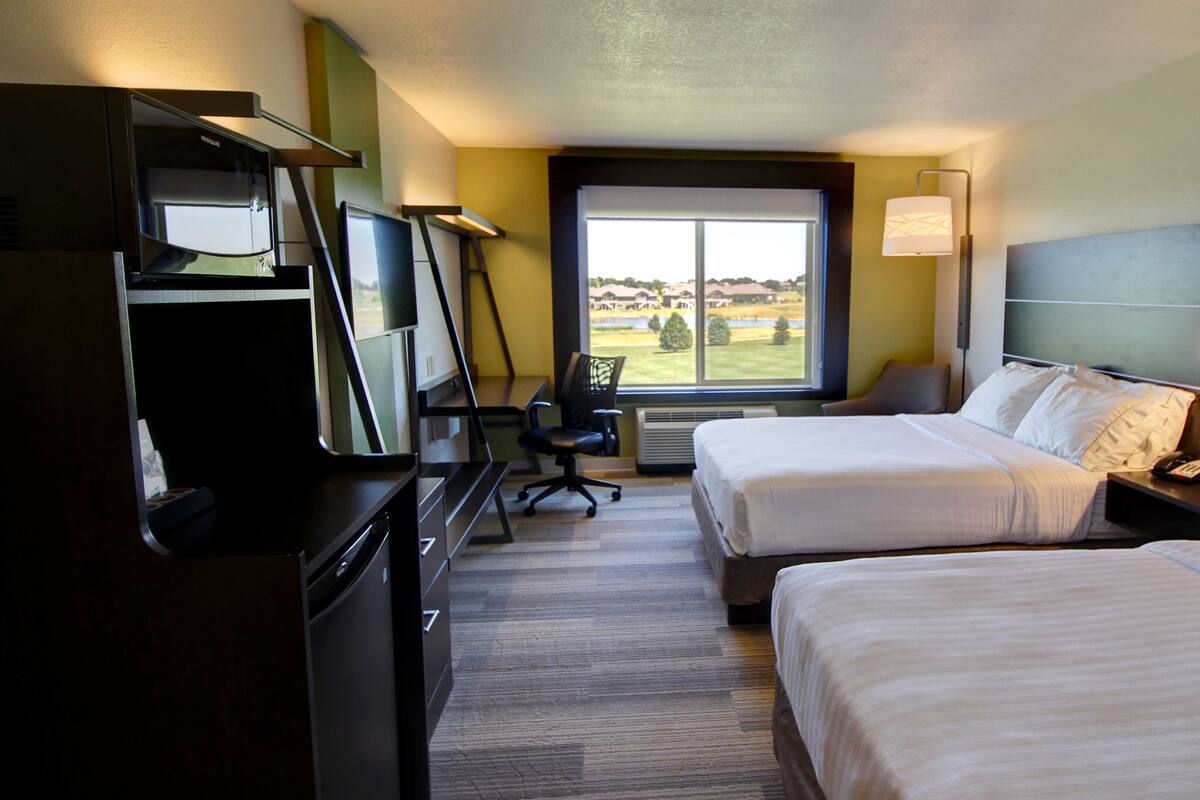 A hotel room with two beds, a desk, a chair, a TV, and a large window with a view of a golf course.