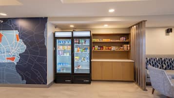 A modern hotel lobby with a map mural, a refrigerated beverage display, a snack bar, and a seating area.