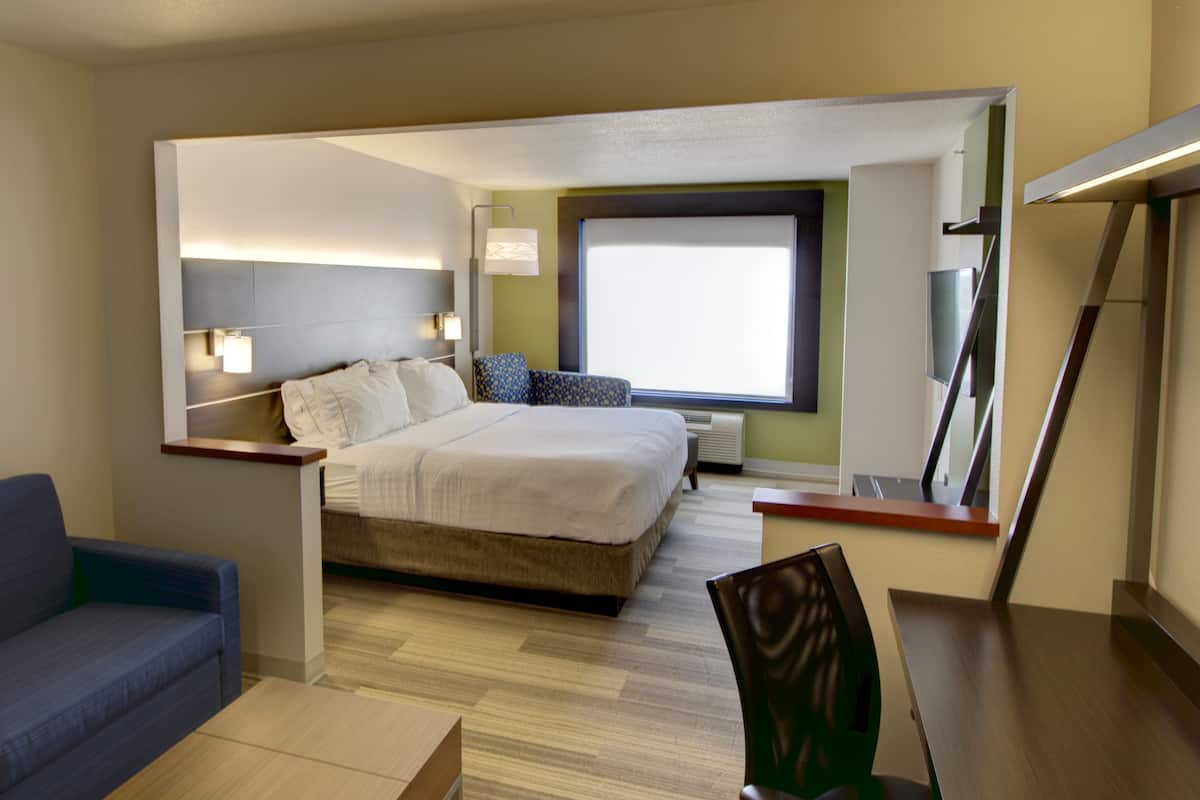 A modern hotel room with a bed, a blue sofa, a desk, and a large window.