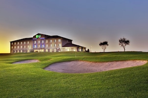 Un hotel Holiday Inn Express con un diseño moderno, ubicado en una colina cubierta de césped con búnkeres de arena.