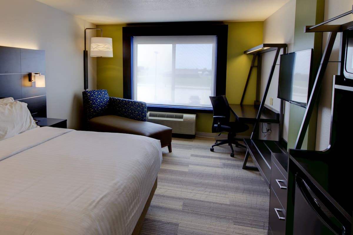 A hotel room with a large bed, a desk, a chair, a TV, and a window with blinds.