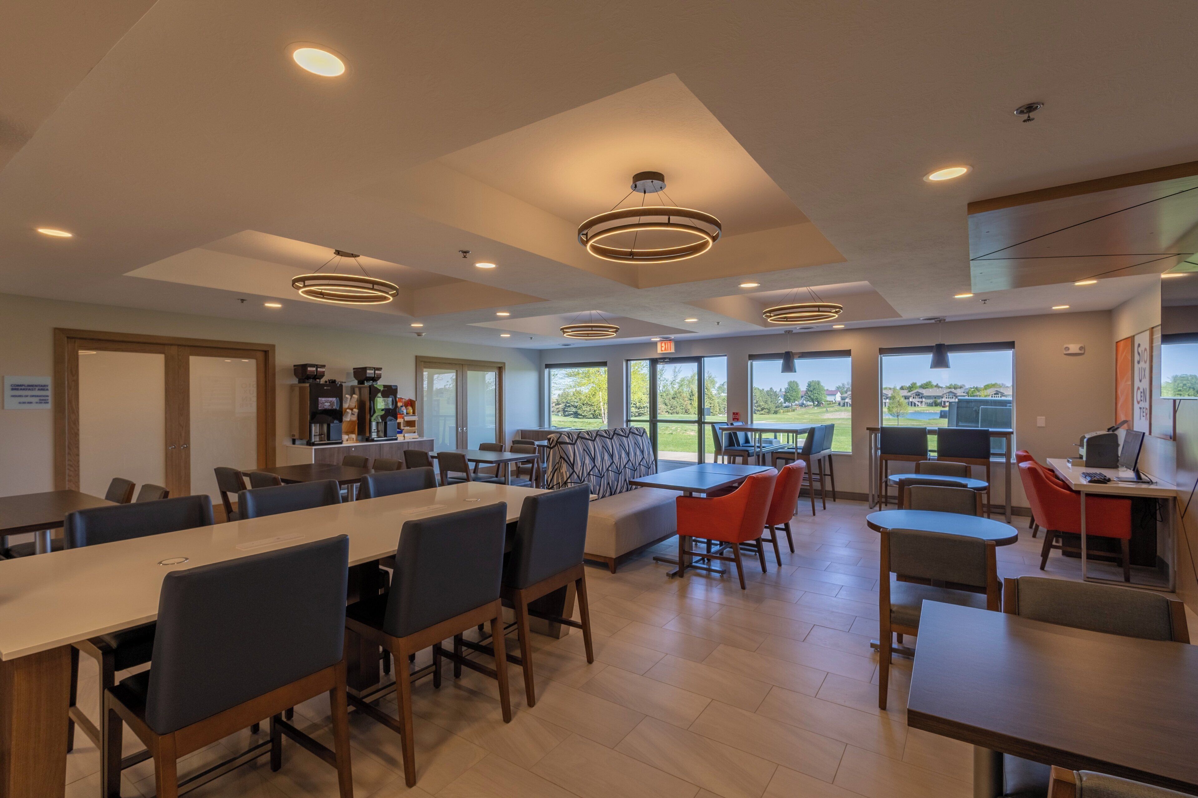 A modern dining area with multiple tables and chairs, a bar area, and large windows offering a view of the outdoors.