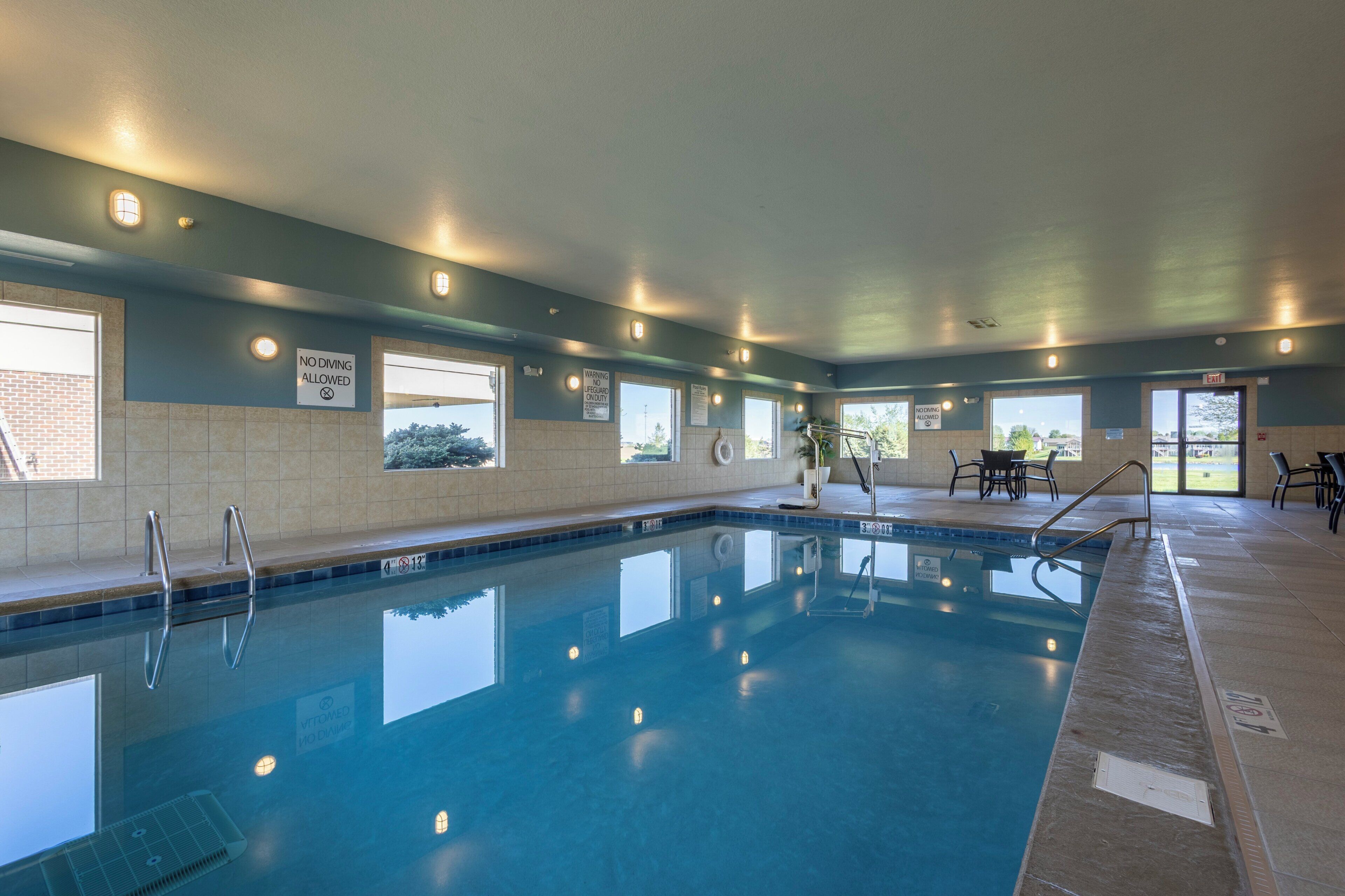 Piscina interna com sinalização clara, piso revestido e área de estar com mesas e cadeiras.