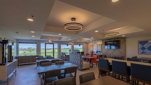 A spacious indoor area with multiple tables and chairs, large windows offering a view of the outdoors, and a television screen mounted on the wall. - Holiday Inn Express & Suites Sioux Center by IHG (Sioux Center)