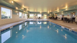 A swimming pool with clear water, surrounded by a lounge area with chairs and tables, and large windows providing natural light. - Holiday Inn Express & Suites Sioux Center by IHG (Sioux Center)