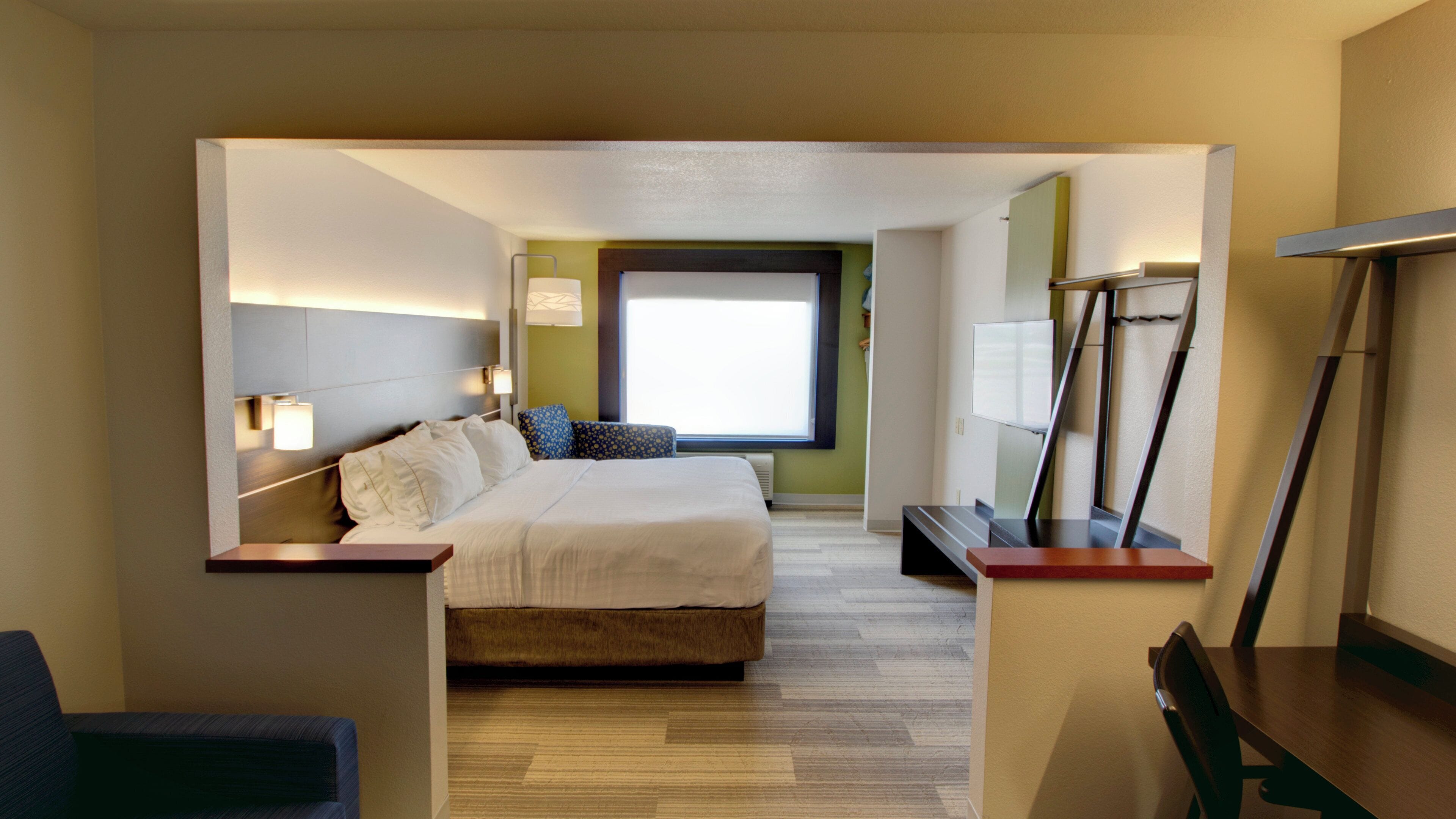 A hotel room with a bed, bedside lamps, a window, a desk, and a chair.