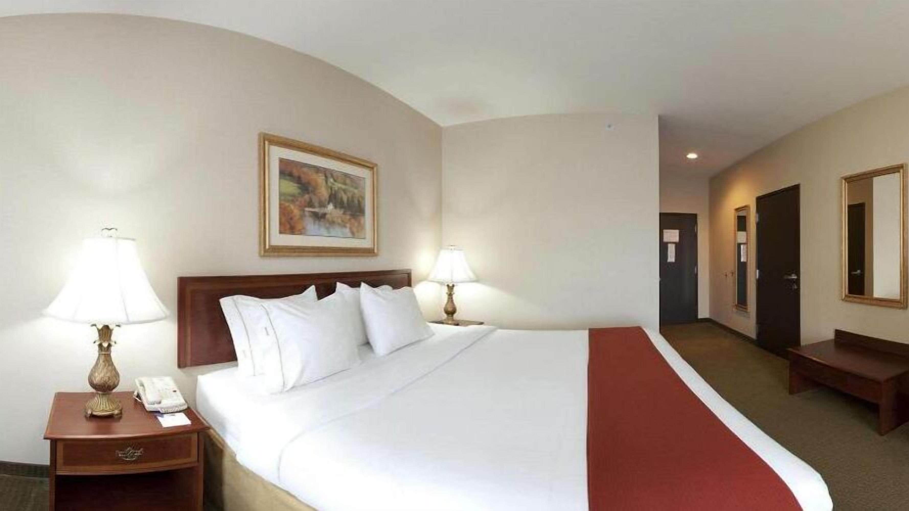 Ein Hotelzimmer mit einem großen Bett, zwei Nachttischlampen, einem Bild an der Wand und einer roten Tagesdecke.