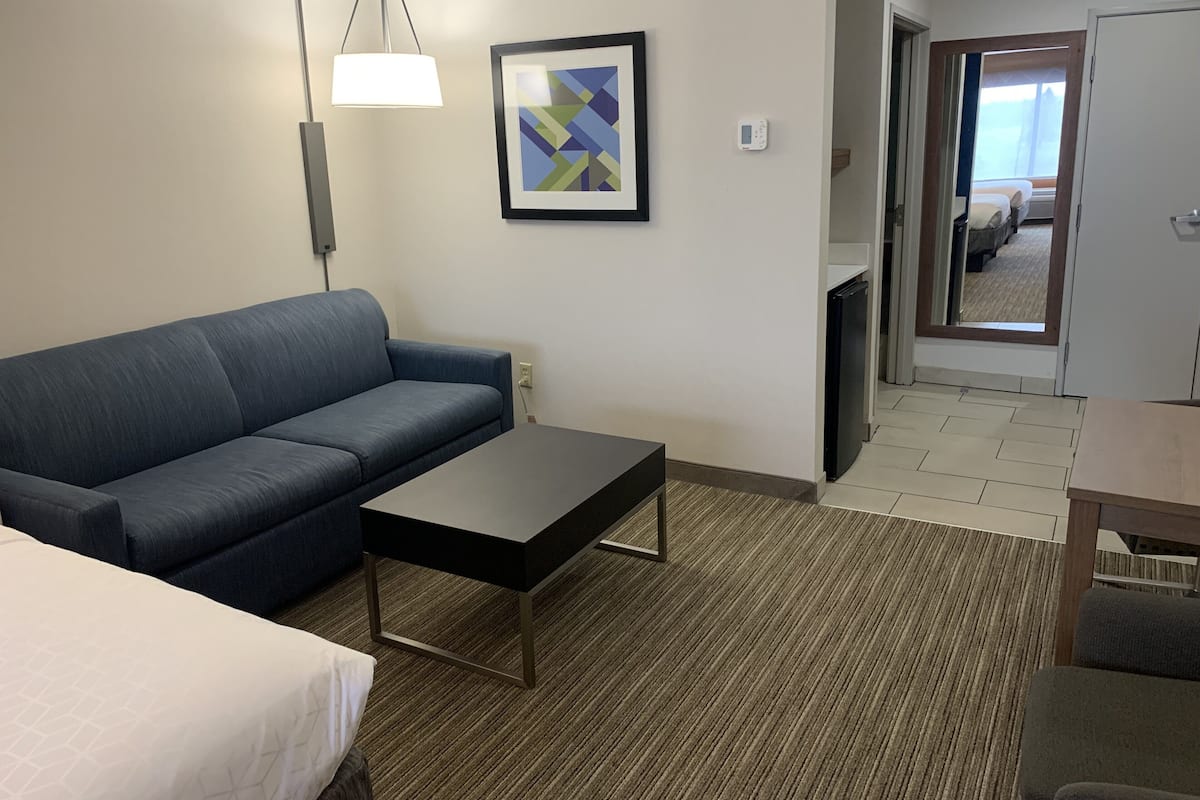 Une chambre d’hôtel avec un canapé, une petite table, une lampe, un tableau encadré et un thermostat.