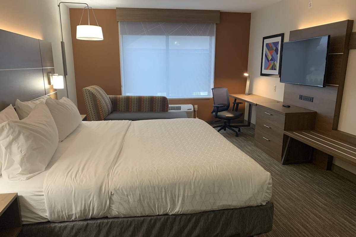 Une chambre d’hôtel avec un grand lit, un bureau, une chaise, une télévision et une fenêtre avec des stores.