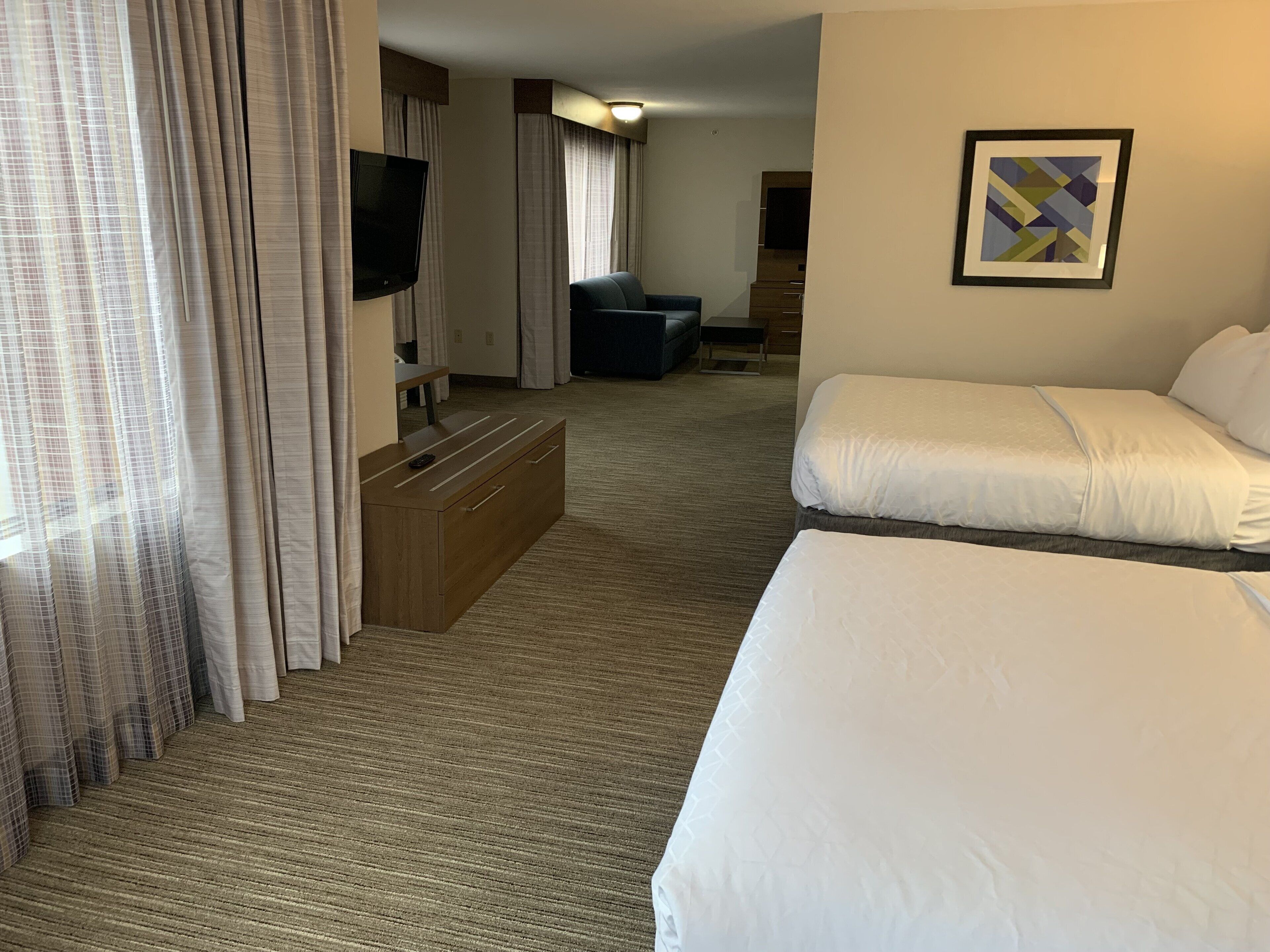 A hotel room with two beds, a TV, a desk, and a couch.