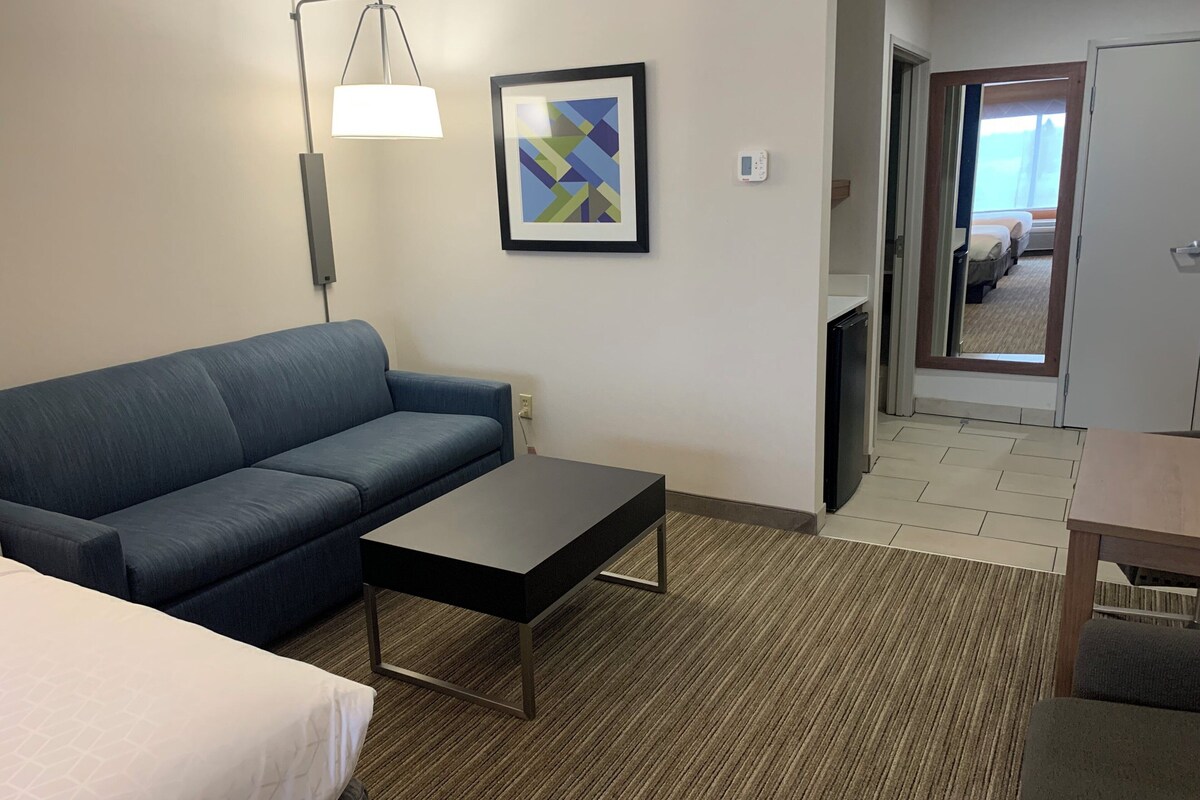 Ein Hotelzimmer mit Sofa, einem kleinen Tisch, einer Lampe, einem gerahmten Bild und einem Thermostat.