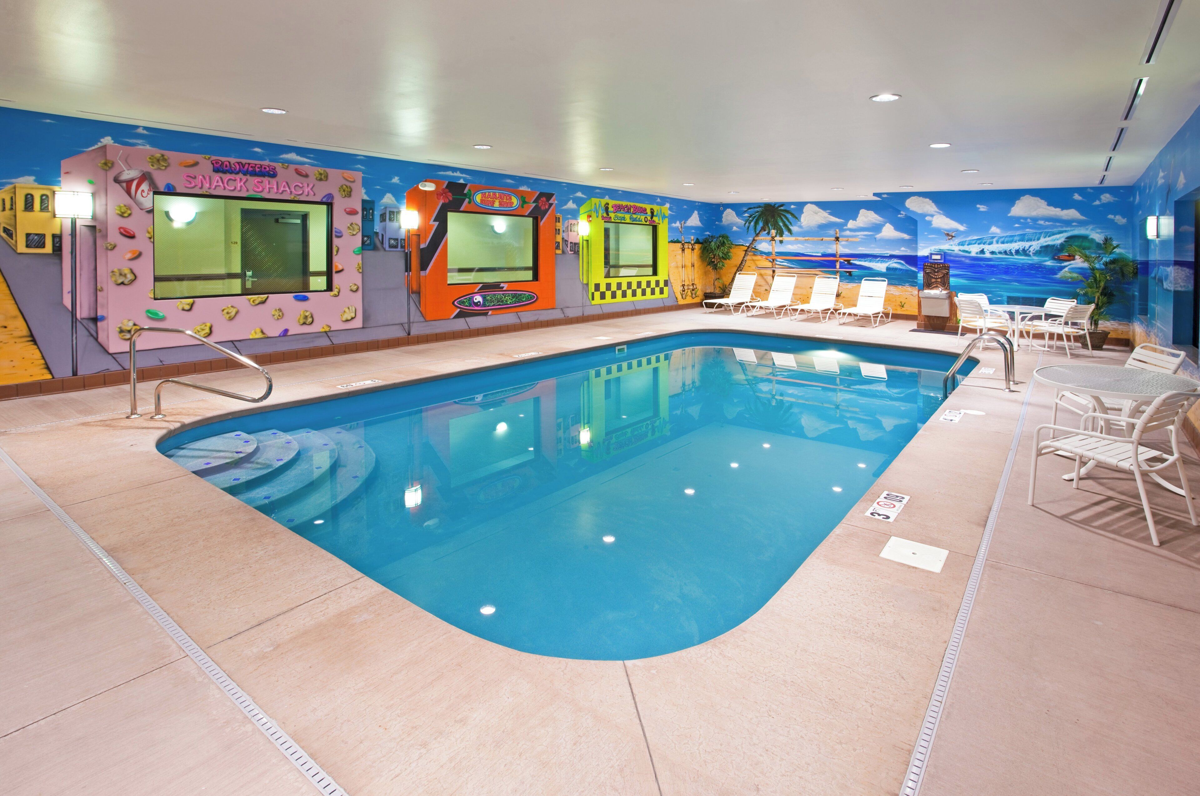 An indoor swimming pool with a colorful mural, lounge chairs, and a snack bar.