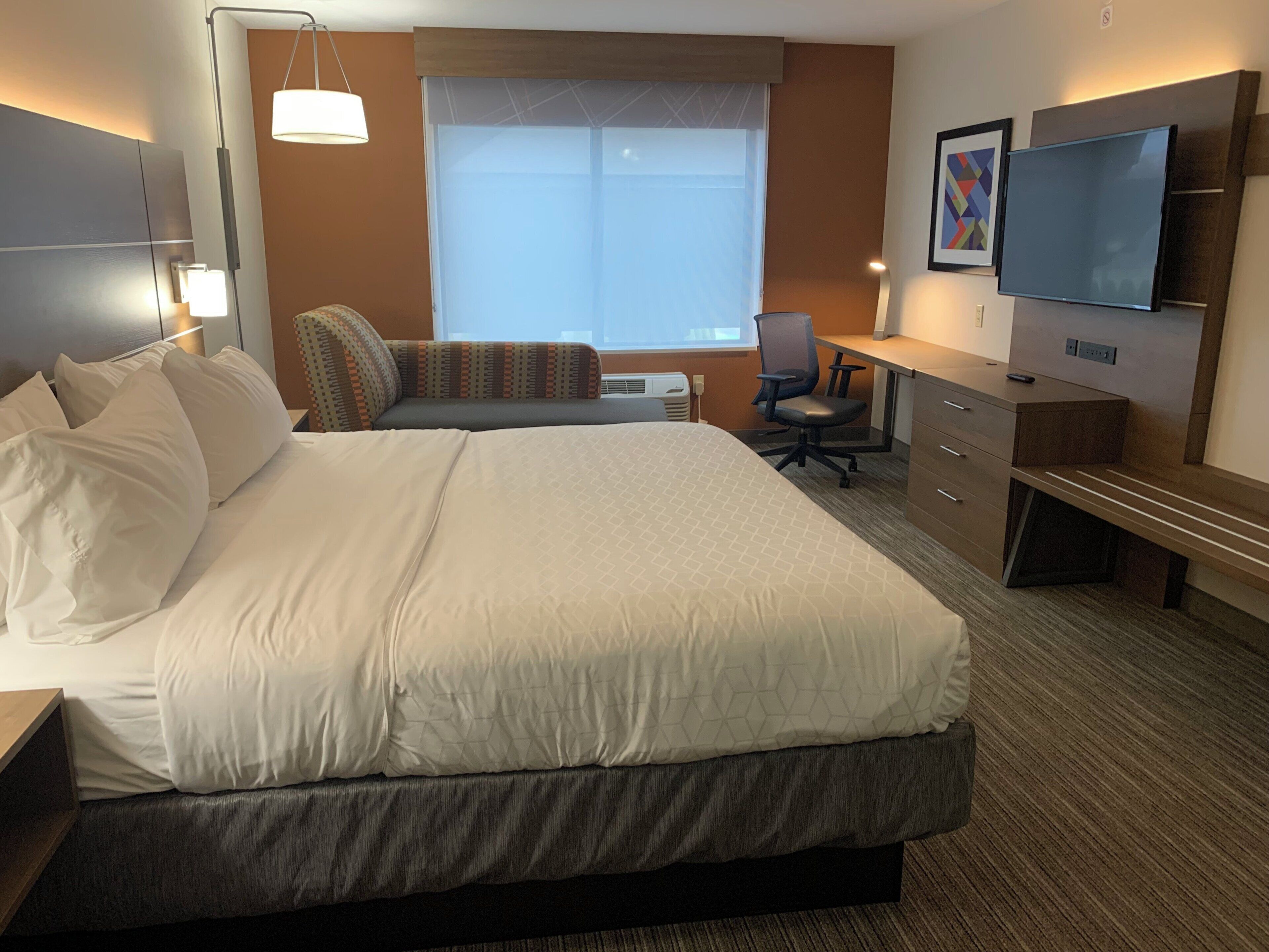 A hotel room with a large bed, a desk, a chair, a television, and a window.