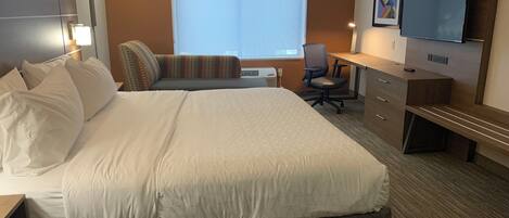 A hotel room with a large bed, a desk, a chair, a television, and a window.