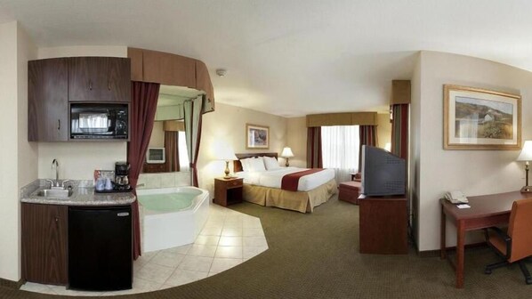 Ein Hotelzimmer mit Küchenzeile, einem eigenen Badezimmer mit Badewanne, einem Bett mit zwei Kissen, einem Schreibtisch mit Stuhl und einem Fernseher.