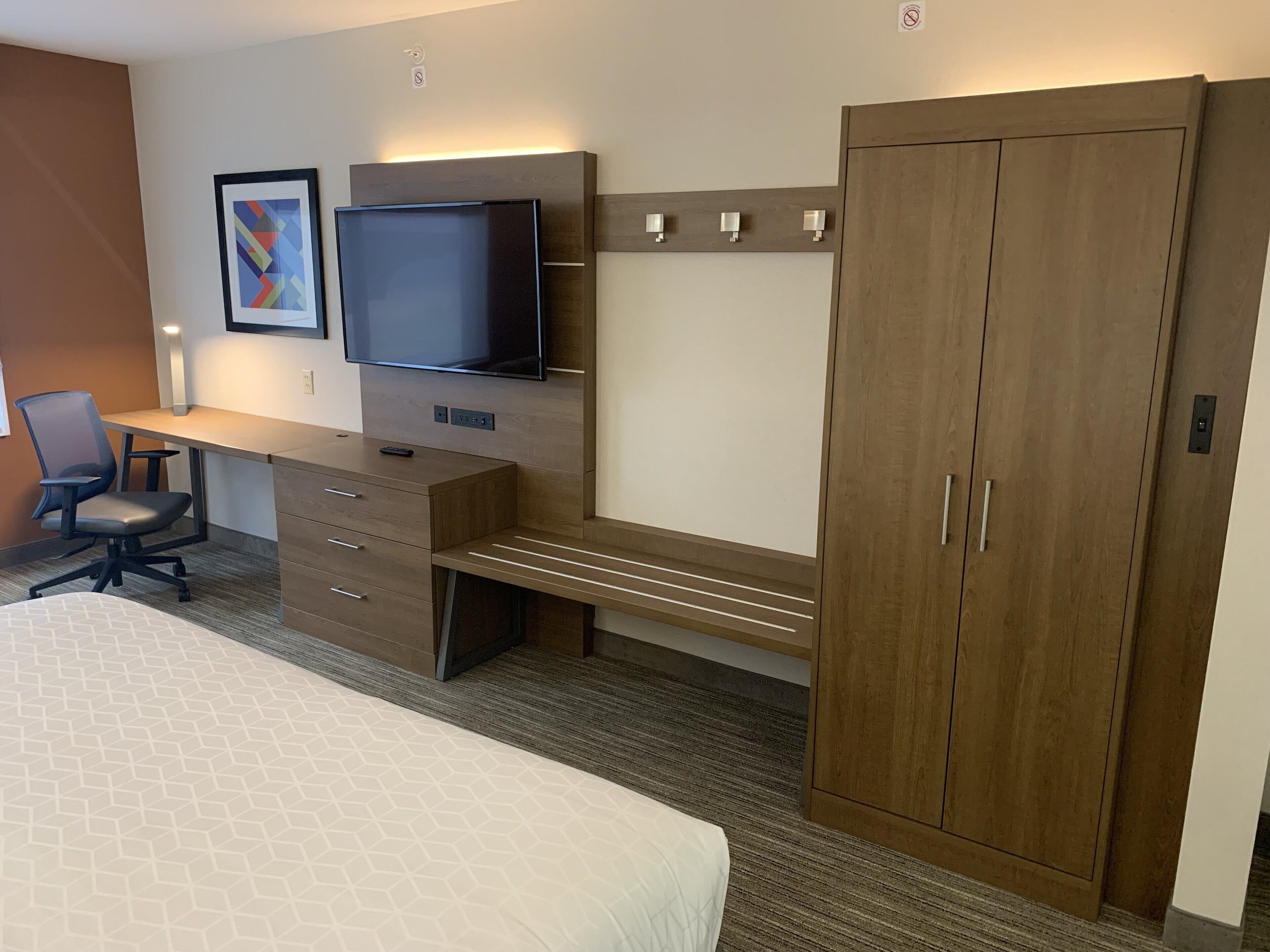 A hotel room with a bed, a desk with a TV, a chair, and a wardrobe.