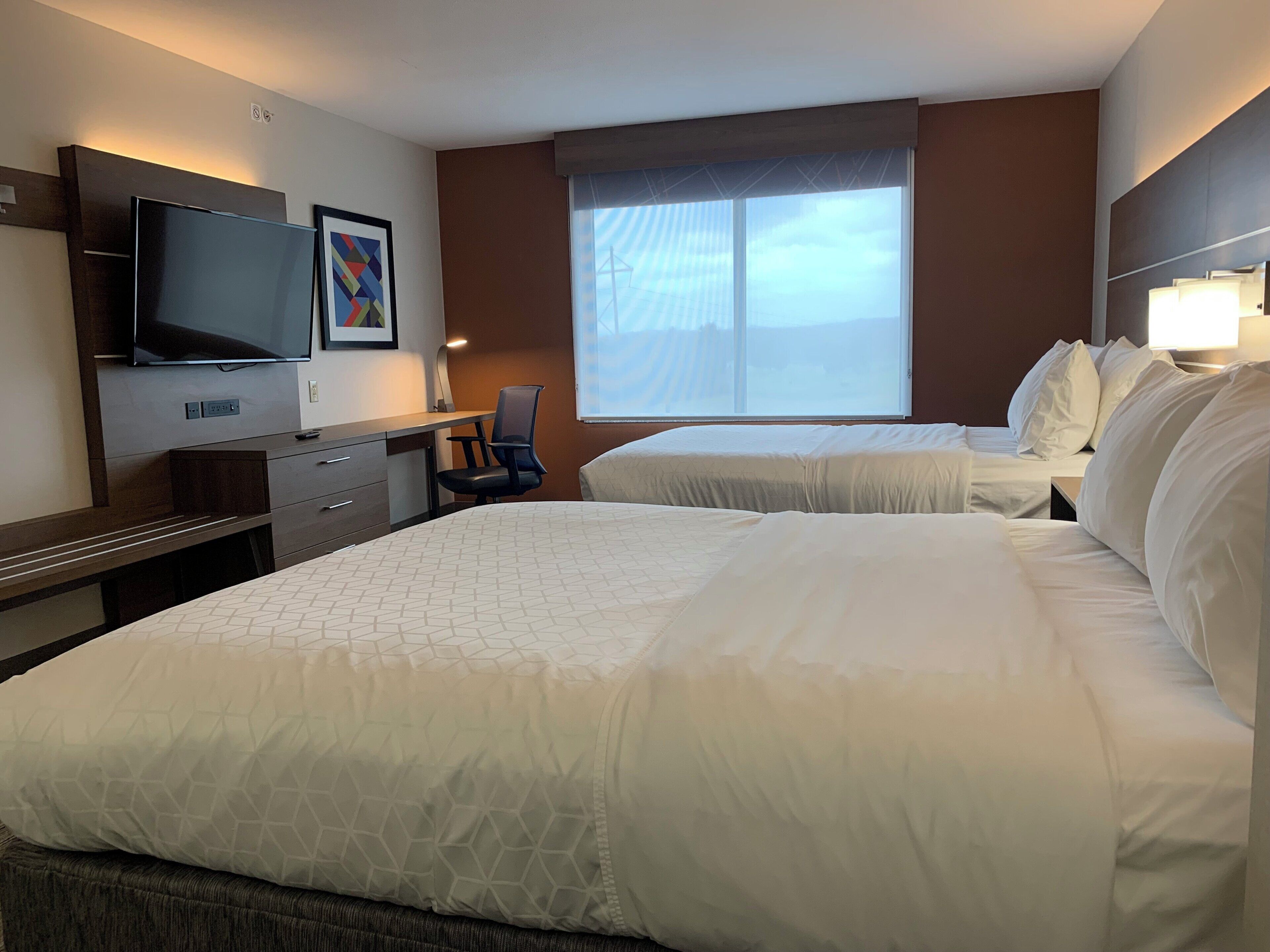 Une chambre d’hôtel avec deux lits, un bureau, une chaise, une télévision et une fenêtre donnant sur un beau paysage.