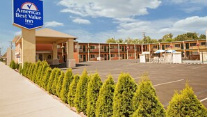 A motel with a sign for 'America's Best Value Inn by Vantage'. It features a parking lot, a building with multiple rooms, and a row of evergreen trees in front.