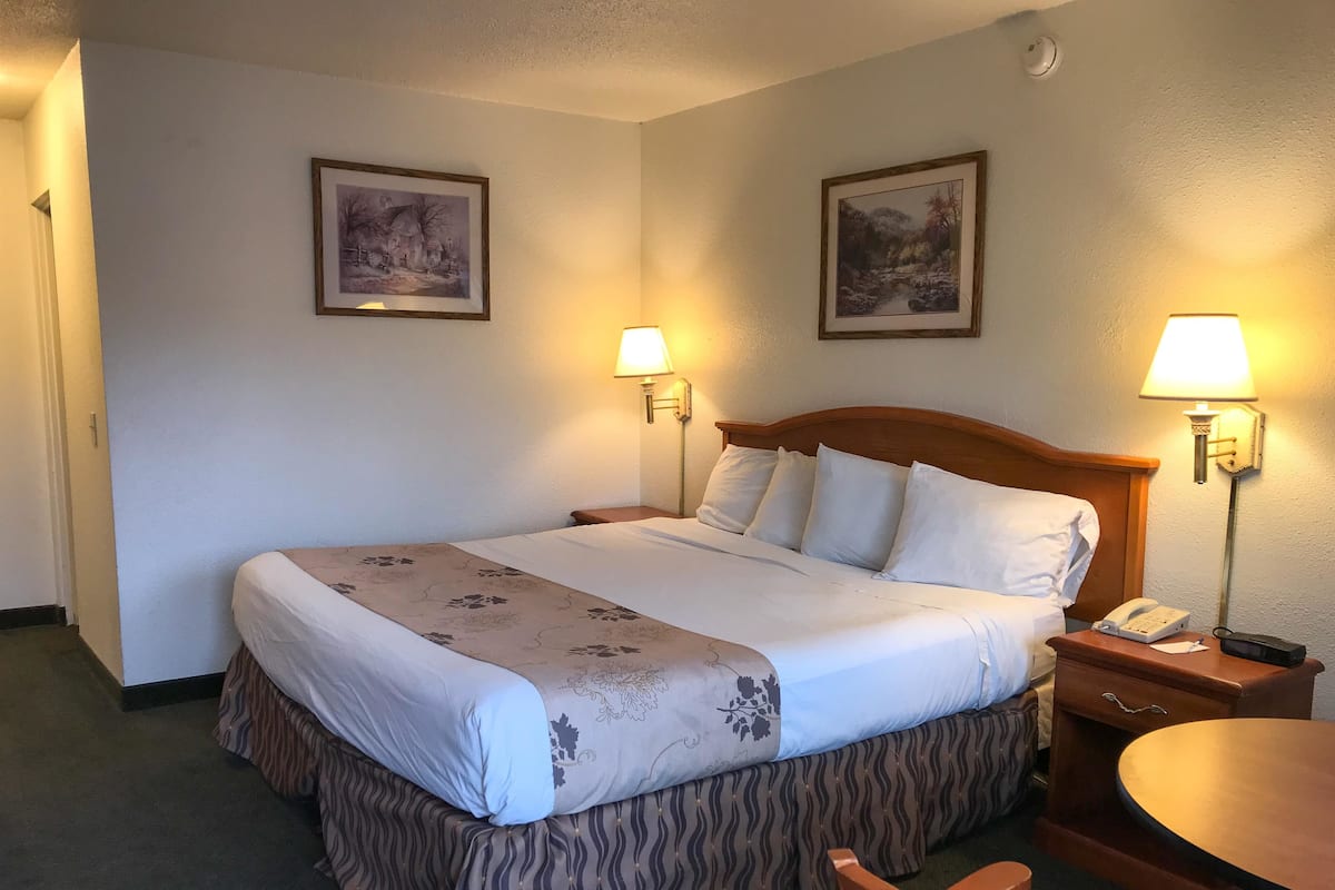 A neatly made bed with a floral bedspread, two wall-mounted lamps, and a small bedside table with a phone and a notepad.