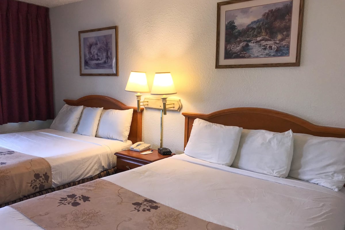 A hotel room with two beds, a nightstand with a lamp, and two framed pictures on the wall.