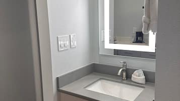 Un baño moderno con un lavamanos blanco, un espejo y una toalla colgada en un perchero.