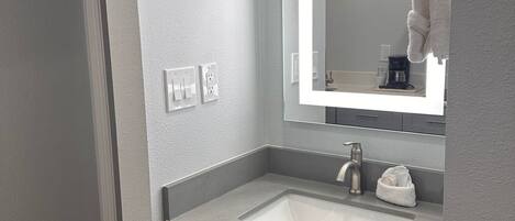 Ein modernes Badezimmer mit einem weißen Waschbecken, einem Spiegel und einem Handtuch an einem Halter.