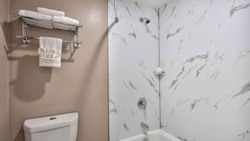 A bathroom with a toilet, a towel rack with towels, and a shower with a marble wall.