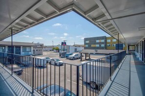 A view from a balcony with a metal railing, overlooking a parking area with several vehicles, including a white pickup truck and a blue car. - Studio 6 Eureka, CA – Old Town (Eureka)