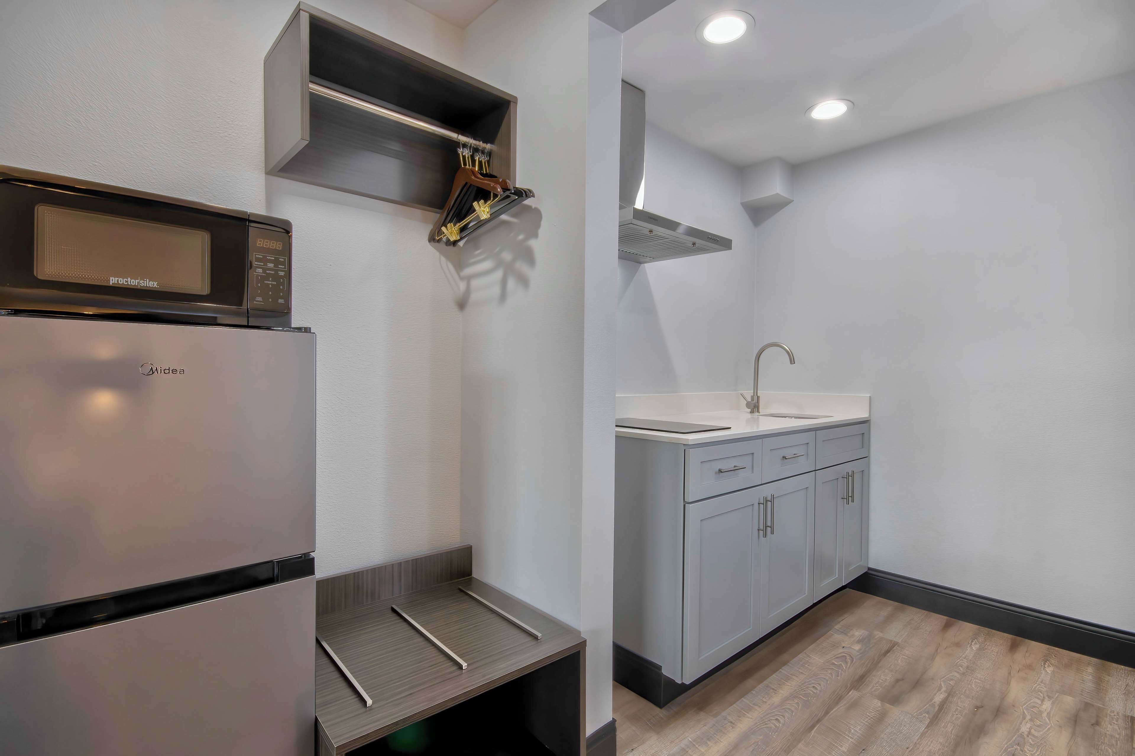 A compact kitchen with a built-in microwave, a stainless steel refrigerator, a sink, and a wooden countertop.