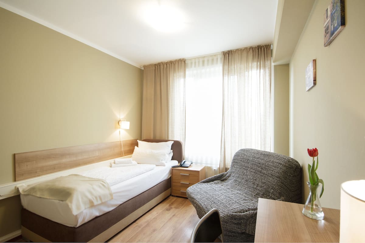 Ein Hotelzimmer mit Bett, Stuhl, Nachttisch, Lampe und einer Vase mit einer Blume.