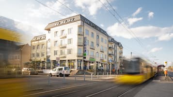 Ein mehrstöckiges Hotel mit Balkonen, einer Straßenbahnlinie und einem Fußweg.