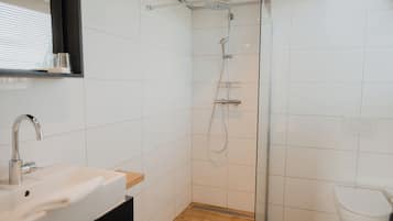 Un baño moderno con ducha de vidrio, lavamanos blanco sobre encimera de madera y un inodoro blanco.