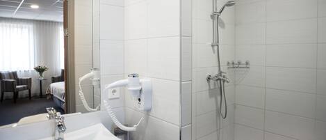 Un baño moderno con lavamanos blanco, cabina de ducha de vidrio y un secador de pelo en la pared.