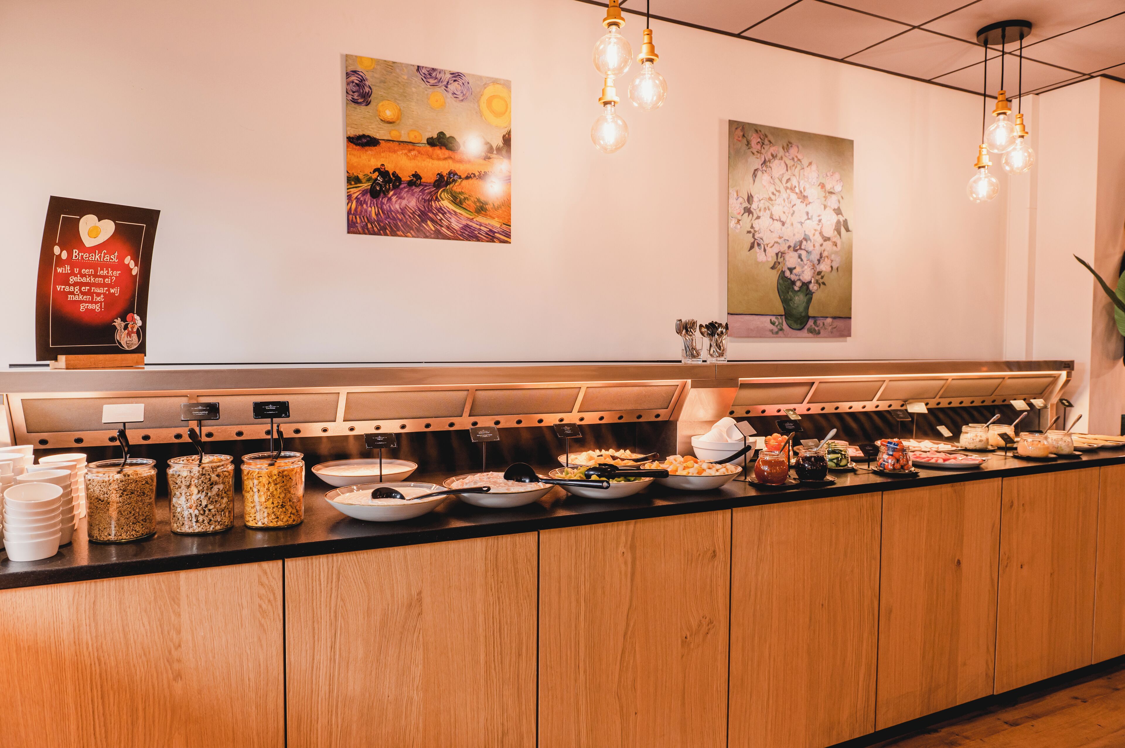 A buffet counter with various food items and a sign with breakfast information.