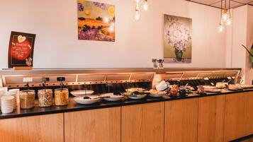A buffet counter with various food items and a sign with breakfast information.