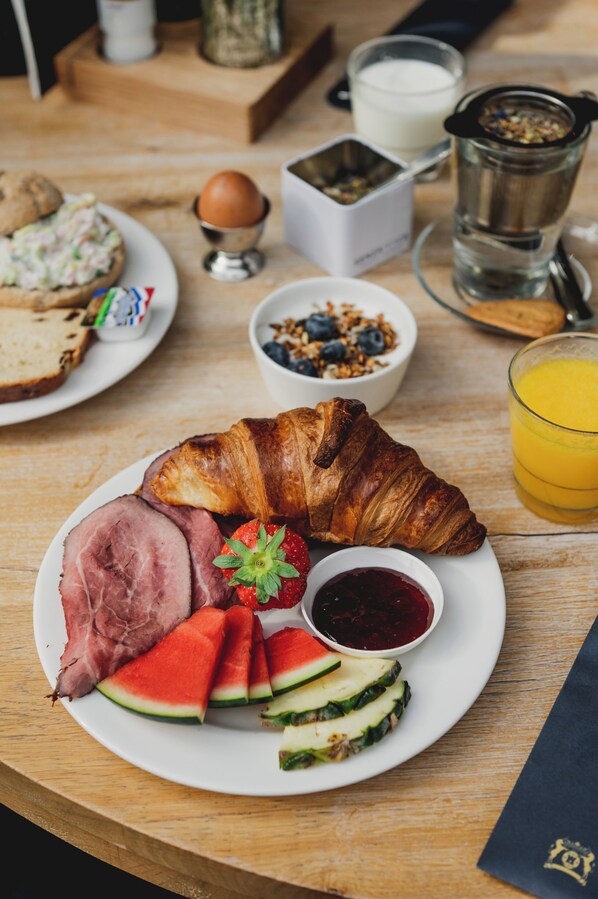 Un plato de desayuno con jamón, croissant, fresas, sandía y rodajas de pepino.