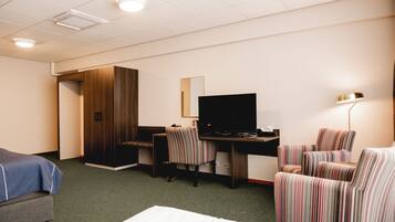 Habitación de hotel con una cama, un escritorio con computadora, un televisor, un sillón a rayas y una lámpara.