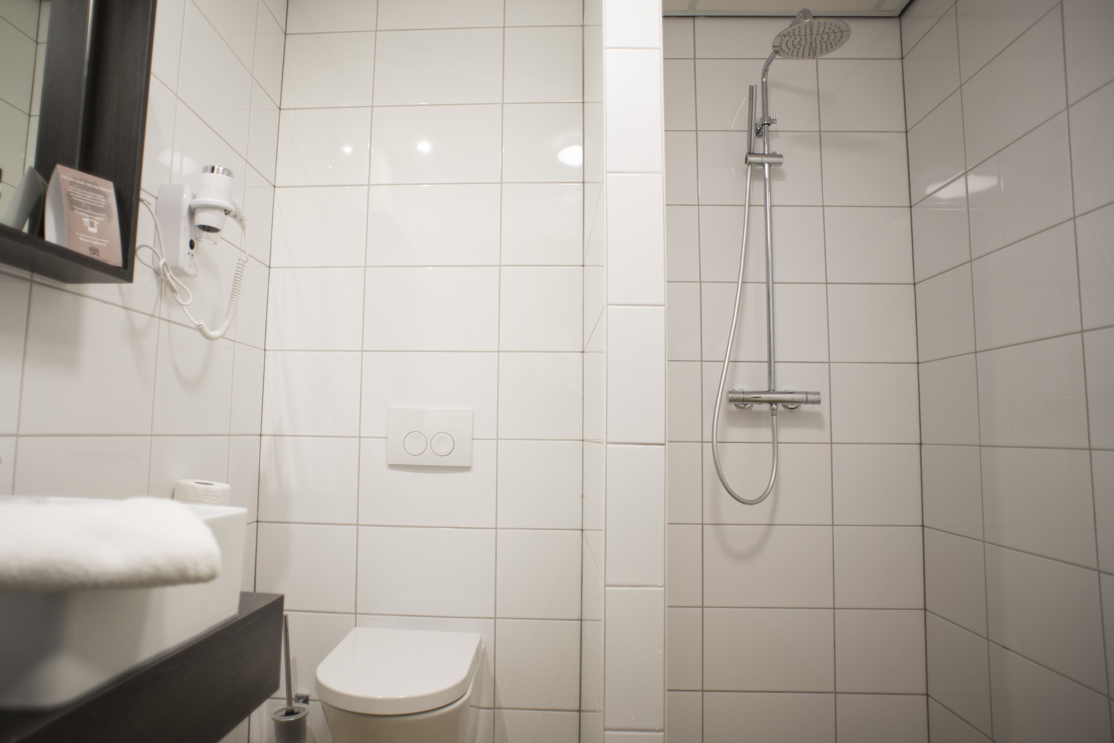 A modern bathroom with a toilet, a sink, a mirror, a hairdryer, and a shower.